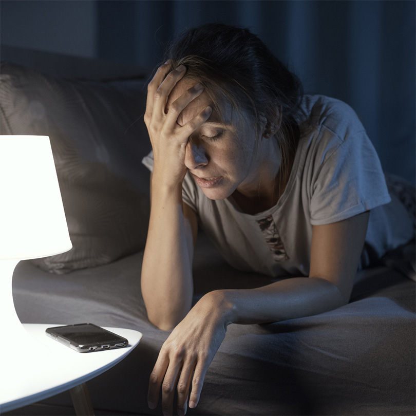woman on bed with head in hand by lamp